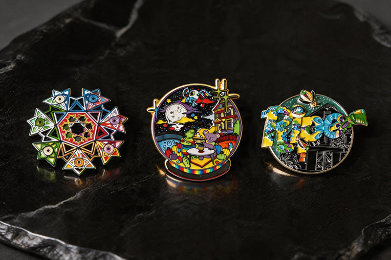 A collection of highly detailed custom hard and soft enamel pins displayed on a dark stone surface.